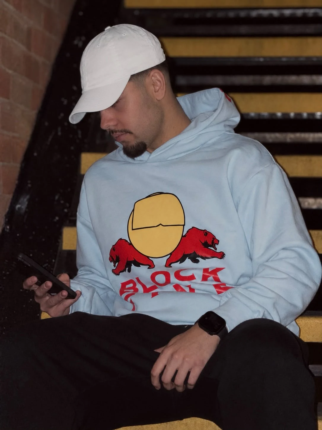Blue NO RUSH hoodie with red and yellow artwork on a staircase